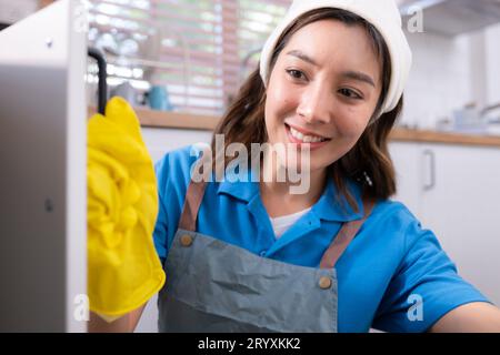 Lächelnde junge Frau in Schürze und Putzhandschuhe öffnen Küchenschränke Stockfoto