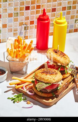 Köstliche hausgemachte Burger auf Holztablett in hellem Sonnenlicht. Burger mit Kalbsschnitzel, Pamidor, Käse, roten Zwiebeln, Salat, aru Stockfoto