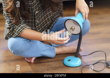 Asiatische Frau wechselt Glühbirne in der Lampenrenovierung mit Ausrüstung zum selbermachen der Glühbirne und Lampe, die auf dem Boden sitzt Stockfoto