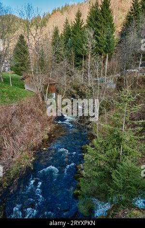 Ein hellblauer Fluss fließt durch einen Wald, während die Sonne in einem versteckten Park entlang der malerischen Fahrt in Süddeutschland untergeht Stockfoto