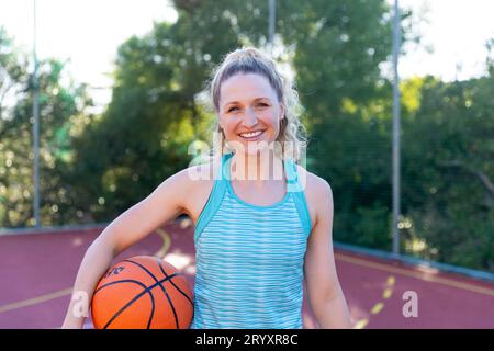 Porträt einer fröhlichen, weißen Basketballspielerin, die Basketball auf dem Basketballplatz hält Stockfoto