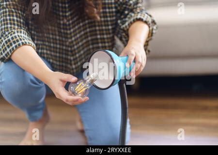 Asiatische Frau wechselt Glühbirne in der Lampenrenovierung mit Ausrüstung zum selbermachen der Glühbirne und Lampe, die auf dem Boden sitzt Stockfoto