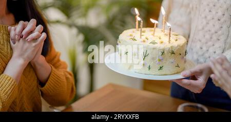 Fröhliche Freunde, die zu Hause Geburtstagsfeier genießen. Asiatische Schwester jubelt Rotwein trinken mit Geburtstagskuchen. Stockfoto