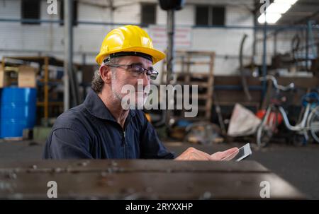Ein älterer Techniker verwendet einen Computer, um die Betriebssteuerung einer Stanzmaschine aus Stahl zu testen. Stockfoto