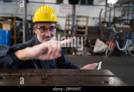 Ein älterer Techniker verwendet einen Computer, um die Betriebssteuerung einer Stanzmaschine aus Stahl zu testen. Stockfoto
