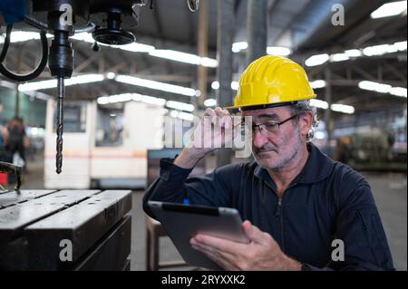 Ein älterer Techniker verwendet einen Computer, um die Betriebssteuerung einer Stanzmaschine aus Stahl zu testen. Stockfoto
