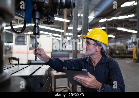 Ein älterer Techniker verwendet einen Computer, um die Betriebssteuerung einer Stanzmaschine aus Stahl zu testen. Stockfoto