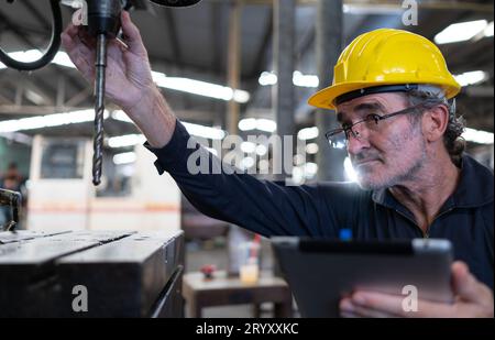 Ein älterer Techniker verwendet einen Computer, um die Betriebssteuerung einer Stanzmaschine aus Stahl zu testen. Stockfoto