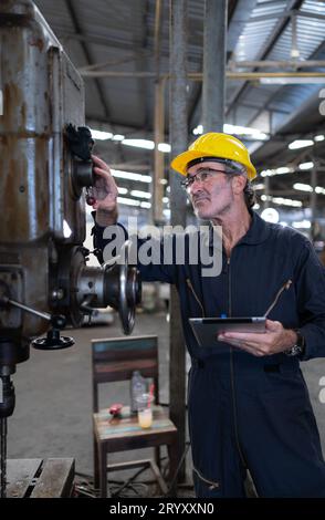 Ein älterer Techniker verwendet einen Computer, um die Betriebssteuerung einer Stanzmaschine aus Stahl zu testen. Stockfoto