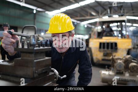 Ein älterer Techniker verwendet einen Computer, um die Betriebssteuerung einer Stanzmaschine aus Stahl zu testen. Stockfoto