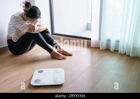 Traurige Frau mit Fettverstimmung gelangweilt von der Diät Gewichtsverlust failÂ Fettdiät und Waage traurige asiatische Frau auf Gewichtswaage zu Hause Gewicht c Stockfoto