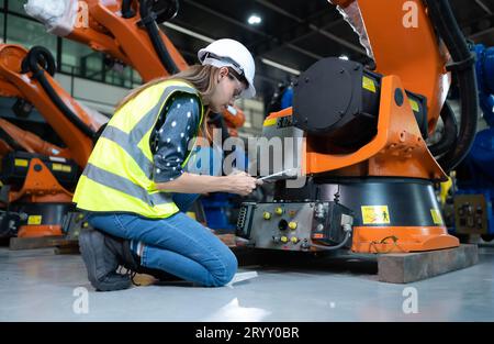 Weibliche Technikerin, die den Roboterarm in einem Roboterhangar inspiziert und repariert und den Betrieb der Maschine nach dem Gebrauch überprüft Stockfoto