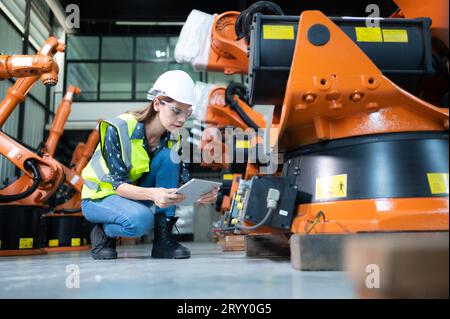 Weibliche Technikerin, die den Roboterarm in einem Roboterhangar inspiziert und repariert und den Betrieb der Maschine nach dem Gebrauch überprüft Stockfoto