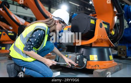 Weibliche Technikerin, die den Roboterarm in einem Roboterhangar inspiziert und repariert und den Betrieb der Maschine nach dem Gebrauch überprüft Stockfoto