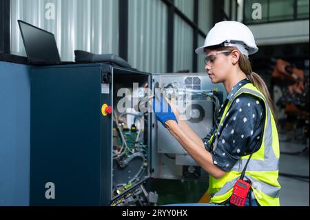Weibliche Technikerin, die den Roboterarm in einem Roboterhangar inspiziert und repariert und den Betrieb der Maschine nach dem Gebrauch überprüft Stockfoto