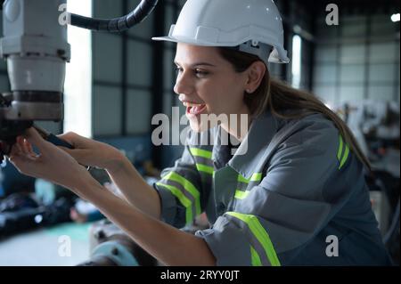 Weibliche Technikerin, die den Roboterarm in einem Roboterhangar inspiziert und repariert und den Betrieb der Maschine nach dem Gebrauch überprüft Stockfoto