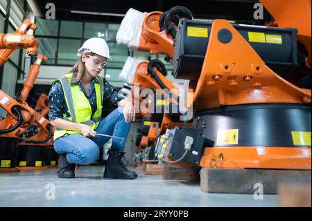 Weibliche Technikerin, die den Roboterarm in einem Roboterhangar inspiziert und repariert und den Betrieb der Maschine nach dem Gebrauch überprüft Stockfoto