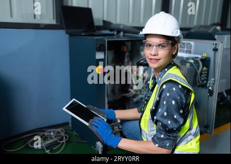 Weibliche Technikerin, die den Roboterarm in einem Roboterhangar inspiziert und repariert und den Betrieb der Maschine nach dem Gebrauch überprüft Stockfoto