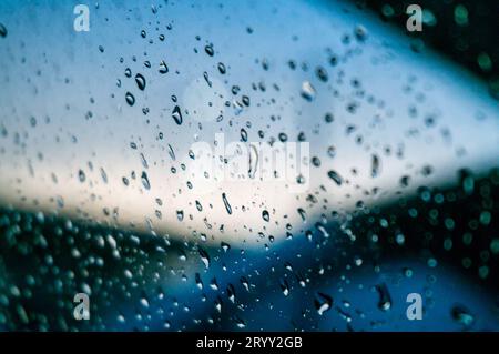 Regen tropft mit Sonnenuntergang auf die Glasoberfläche. Tropfen auf Glasspray auf Fensterhintergrund für dunkle textÂ selektive Fokussierung Stockfoto