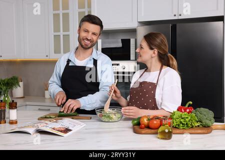 Glückliches Paar, das Rezept im Kochmagazin liest, während er zu Hause kocht Stockfoto