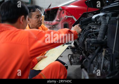 Beide Automechaniker prüfen den Motor eines Kundenfahrzeugs, das zur Reparatur in einer Werkstatt gebracht wird. Stockfoto