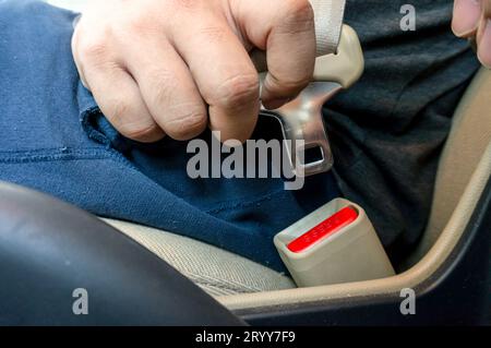 Mann, der die Hände mit dem Sicherheitsgurt im Fahrzeug anschnallt (Sicherheitsgurt), selektiver Fokus. Sicherheitsfahrkonzept. Stockfoto