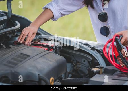 Großaufnahme einer Frau, die das Batteriekabel hält, Kupferdraht für die Reparatur eines defekten Fahrzeugs hält, indem die Batterie mit der roten und schwarzen Linie an e angeschlossen wird Stockfoto