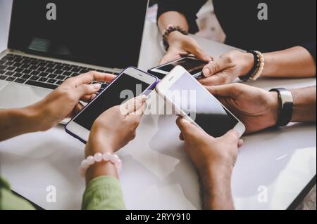 Gruppe junger Hipster mit Handys in der Hand im Büro mit Laptop-Hintergrund. Freunde, die gemeinsam Spaß haben, wi Stockfoto