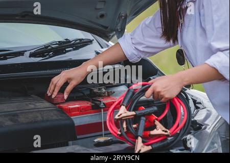 Großaufnahme einer Frau, die das Batteriekabel hält, Kupferdraht für die Reparatur eines defekten Fahrzeugs hält, indem die Batterie mit der roten und schwarzen Linie an e angeschlossen wird Stockfoto