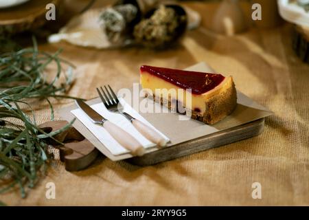 Eine Nahaufnahme eines Erdbeerkäsekuchenschnitts auf einem rustikalen Holzbrett, mit der sanften Umarmung von Kerzenlicht, präsentiert auf einem Sackleinen ta Stockfoto