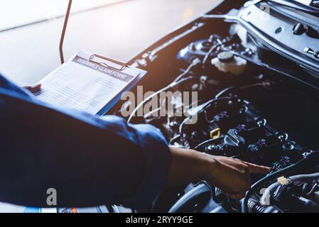 Kfz-Mechaniker hält Clipboard und überprüft das Wartungsfahrzeug durch Kundenversicherungsauftrag in der Autowerkstatt. Stockfoto