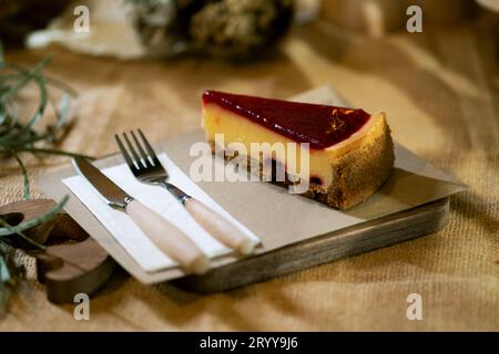 Eine Nahaufnahme eines Erdbeerkäsekuchenschnitts auf einem rustikalen Holzbrett, mit der sanften Umarmung von Kerzenlicht, präsentiert auf einem Sackleinen ta Stockfoto