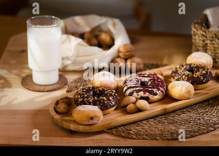 Auf einem Holzteller locken drei Donuts, mit Schokolade gefüllte Kekse und kleine Kekse. Mit einem weißen Tuch, einem Haufen Walnüsse und einem Ref Stockfoto