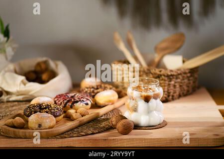 Auf einer Holzplatte befinden sich Donuts, mit Schokolade gefüllte Kekse und kleine Kekse. Dahinter liegen Walnüsse auf einem weißen Tuch, mit Holzutensilien in einem Docht Stockfoto