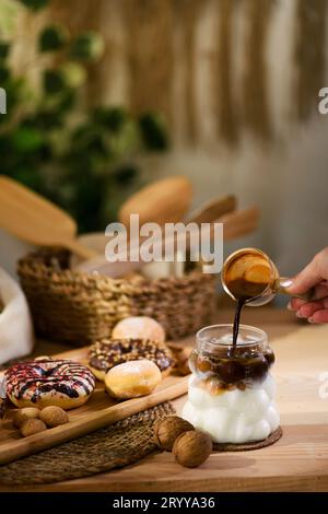 Ein Schnappschuss, der den Moment feststellt, in dem eine Frau Espresso aus einer Kaffeekanne aus Glas in ein mit Eismilch gefülltes Glas gießt. Stockfoto