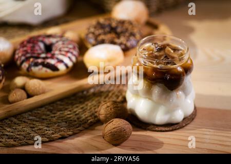 Auf einer Holzplatte befinden sich Donuts, mit Schokolade gefüllte Kekse und kleine Kekse. Dahinter liegen Walnüsse auf einem weißen Tuch, mit Holzutensilien in einem Docht Stockfoto