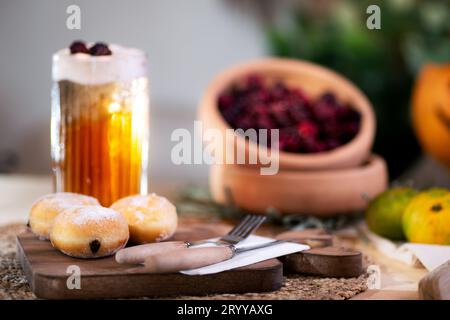 Mit Schokolade gefüllter Keks mit Besteck auf einem Schneidebrett, serviert mit aufschäumendem Apfelsaft, roten Brombeeren, Mandarinen und einer Jack o'Laterne im bac Stockfoto