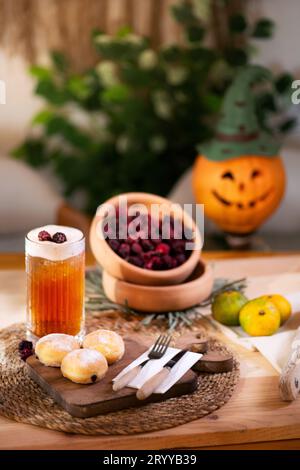 Mit Schokolade gefüllter Keks mit Besteck auf einem Schneidebrett, serviert mit aufschäumendem Apfelsaft, roten Brombeeren, Mandarinen und einer Jack o'Laterne im bac Stockfoto