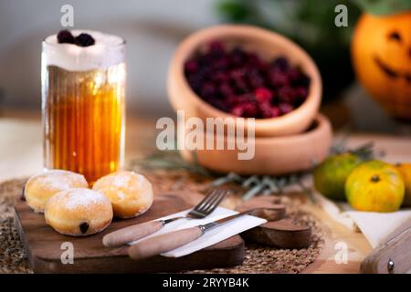 Mit Schokolade gefüllter Keks mit Besteck auf einem Schneidebrett, serviert mit aufschäumendem Apfelsaft, roten Brombeeren, Mandarinen und einer Jack o'Laterne im bac Stockfoto