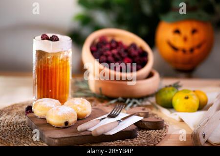 Mit Schokolade gefüllter Keks mit Besteck auf einem Schneidebrett, serviert mit aufschäumendem Apfelsaft, roten Brombeeren, Mandarinen und einer Jack o'Laterne im bac Stockfoto