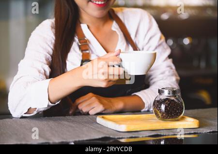 Nahaufnahme einer weißen Kaffeetasse mit einer schönen asiatischen Frau Barista Hintergrund für das Servieren an die Gäste. Tätigkeit und Beruf. Essen und Stockfoto