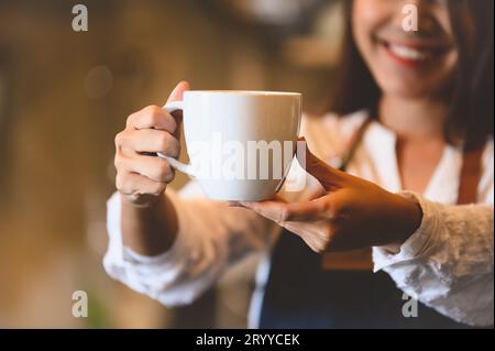 Nahaufnahme einer weißen Kaffeetasse mit einer schönen asiatischen Frau Barista Hintergrund für das Servieren an die Gäste. Tätigkeit und Beruf. Essen und Stockfoto