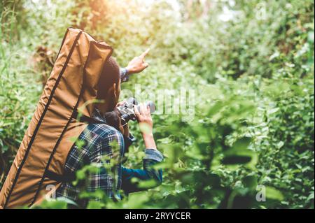 Ein paar asiatische Menschen, die ein Fernglas im Wald halten und sich auf das Ziel freuen. Lebensstil und Freizeitaktivitäten der Menschen Stockfoto