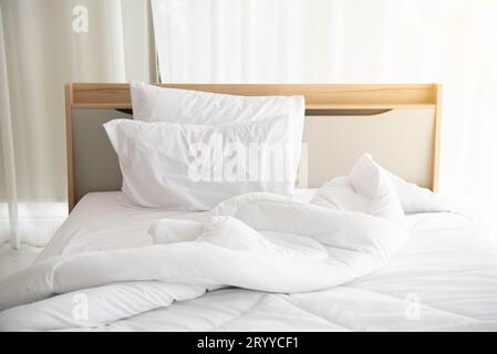 Weißes, ungebautes Bett am Morgen mit Sonnenschein mit weißem Vorhanghintergrund in elegantem Haus. Inneneinrichtung und luxuriöse Möbel Stockfoto