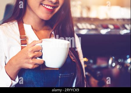 Nahaufnahme eines professionellen weiblichen Baristas, der eine Tasse Kaffee in der Hand macht und hält. Glückliche junge Frau an der Theke im Restaurant Stockfoto