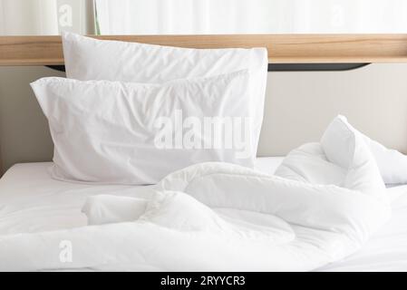 Weißes, ungebautes Bett am Morgen mit Sonnenschein mit weißem Vorhanghintergrund in elegantem Haus. Inneneinrichtung und luxuriöse Möbel Stockfoto