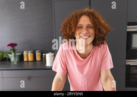 Porträt eines glücklichen birassischen Mannes mit lockigem rotem Haar, der in der modernen Küche auf der Theke liegt Stockfoto