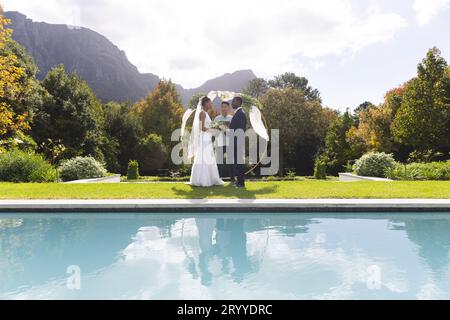 Fröhlicher, vielseitiger Beamter, Braut und Bräutigam bei einer Hochzeit im Freien am Pool im sonnigen Garten, Kopierbereich Stockfoto