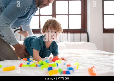 Vater und kleiner Junge haben Spaß beim Spielen mit deinen neuen Spielzeugen im Schlafzimmer. Spielzeug, das die Denkfähigkeit von Kindern verbessert Stockfoto