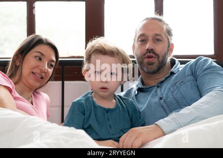Nachdem der kleine Junge aus seinem Nickerchen aufwacht, machen Vater und Mutter in seinem Schlafzimmer angenehme Aktivitäten. Stockfoto